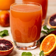 two glasses filled with blood orange juice and garnished with fresh basil leaves next to sliced blood oranges