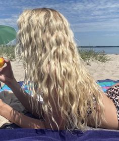 a blonde woman sitting on top of a beach holding an orange