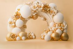 a white and gold arch with flowers on the top is surrounded by balloons, balls, and other decorations