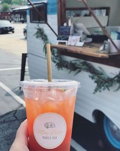 a person holding up a drink in front of a food truck with a straw sticking out of it