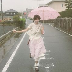 a woman is walking down the street with an umbrella in her hand and she is smiling at the camera