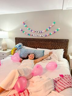 a woman laying on top of a bed covered in pink and white balloons next to a string of lights