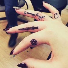 two fingers with tattoos on them, one has an arrow and the other has a cross