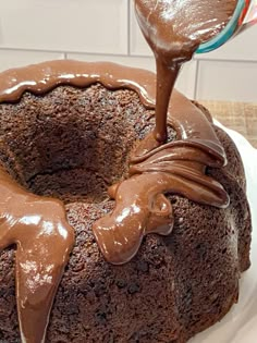 a chocolate bundt cake is being drizzled with chocolate icing on a white plate