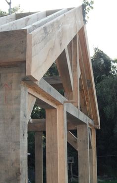 an unfinished house with wooden framing and roof beams on the side of it, in front of some trees