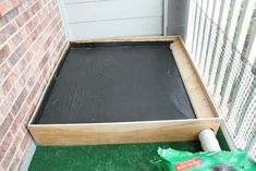 an empty wooden box sitting on top of a green grass covered ground next to a brick wall