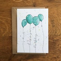 a card with blue balloons floating in the air on top of a wooden table next to a