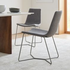 two gray chairs sitting on top of a white rug next to a table with a bowl