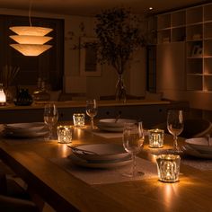 a dining room table is set with place settings and lit candles in front of it