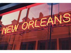 a neon sign that reads new orleans on the side of a store front window with red trim