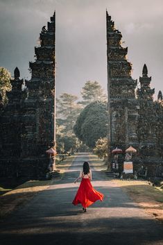 a woman in a red dress is walking down the road towards an old stone gate