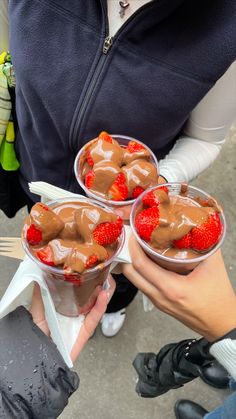 three people are holding cups with chocolate pudding and strawberries