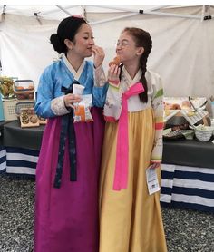 two women in long dresses standing next to each other near a table with food on it