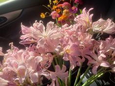 a bunch of pink flowers are in a vase on the dashboard of a car,