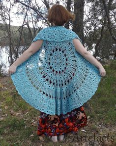 a woman wearing a blue crocheted shawl standing in the grass with her back to the camera