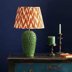 a green lamp sitting on top of a wooden table next to a candle and a blue wall