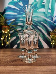 three glasses sitting on top of a wooden table next to a wall with palm leaves