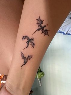 a woman's arm with a tattoo on it that has two bats flying through the air