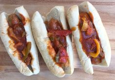 three hot dogs with toppings sitting on top of a wooden cutting board