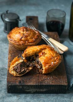 two pastries sitting on top of a wooden cutting board next to some wine glasses