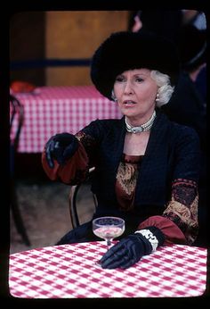 a woman sitting at a table with a glass of wine in her hand and wearing black gloves