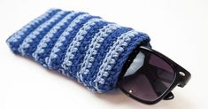 a blue and white crocheted hat with sunglasses on it's side, resting on top of a pair of black sunglasses