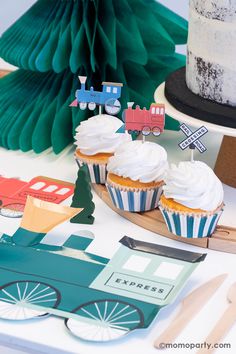 cupcakes with white frosting and train decorations are on a table next to other items