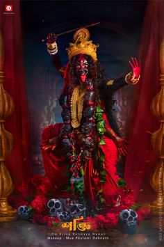 a statue of the hindu god in red and gold with his hands up, surrounded by skulls