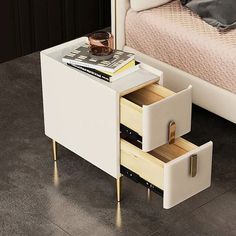 a small white table with two drawers and a book on it next to a bed