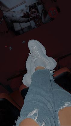 the person is wearing white sneakers and ripped denim pants, while they are sitting in a theater