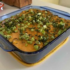 a casserole dish with green onions and cheese in it sitting on a table