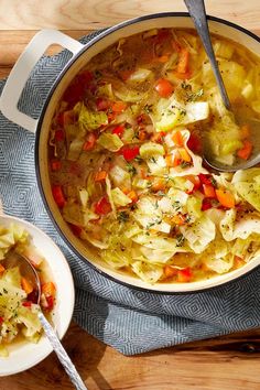 a pot filled with cabbage and carrots on top of a wooden table next to a spoon