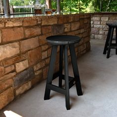 an outdoor bar with two stools next to a stone wall and trees in the background