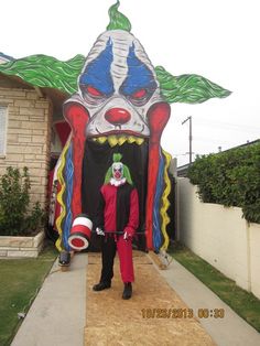 a man standing in front of a giant clown costume on the sidewalk next to a house