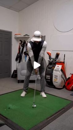 a man hitting a golf ball on the green in a room with other golf equipment