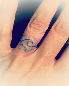 a woman's hand with a small wave tattoo on the middle finger and an aqua blue ring