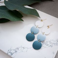 three pairs of earrings sitting on top of a marble table next to a green leaf