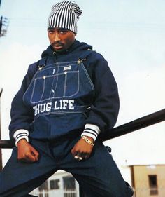 a man sitting on top of a metal rail wearing a blue jacket and striped hat