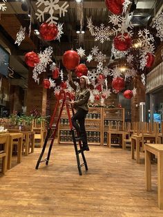 a man is standing on a ladder with red and white ornaments hanging from the ceiling