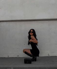 a woman kneeling on the ground with her legs crossed, wearing black boots and sunglasses