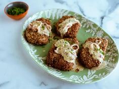 four crab cakes on a green plate with white sauce and garnishes next to a small bowl