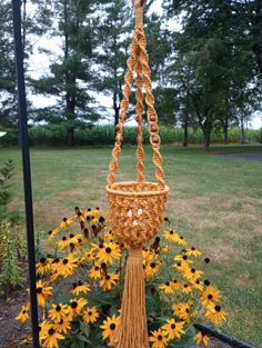 a basket hanging from the side of a pole with flowers in front of it and trees in the background