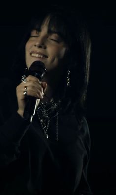 a woman singing into a microphone in the dark