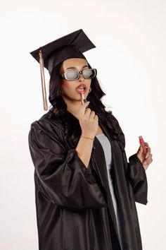 a woman in graduation cap and gown holding her finger up to her mouth while wearing sunglasses