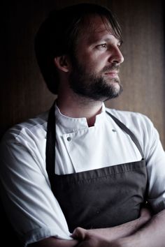 a man wearing an apron and standing in front of a window with his arms crossed