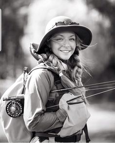 a woman with a hat and bow in her hands smiles at the camera while wearing a backpack