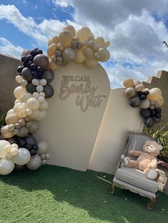 a teddy bear sitting on a chair in front of a balloon arch