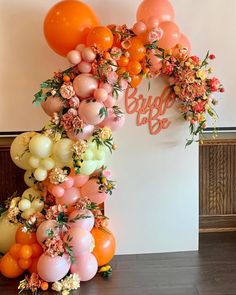 an orange and pink balloon arch is decorated with flowers, leaves and balloons for a bridal party