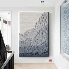 a large painting hanging on the wall next to a stair case in a white room