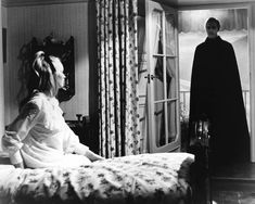 a woman sitting on top of a bed next to a man in a black suit